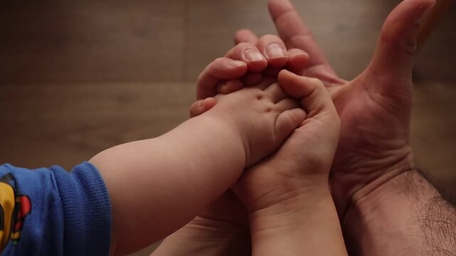 Family hands of baby, child and parents slowly releasing grip and opening palms, symbolizing freedom, growth and gentle separation while maintaining emotional connection in warm light.