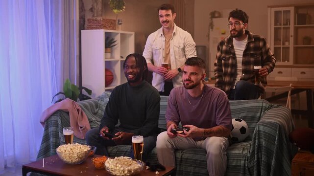 Cheerful multicultural friends celebrating victory while playing video games and drinking beer at home