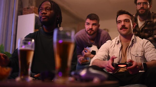 Group of male friends playing video games together and drinking beer at home during a party