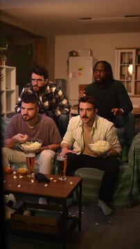 Variety of male buddies showing dismay and irritation as they watch a thrilling sports game on television in a cozy living space
