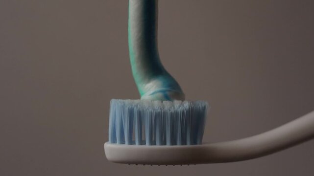 Macro shot of applying toothpaste on a toothbrush, focusing on oral care preparation and hygiene habits. Minimalistic composition with clear detail of texture and daily dental routine concept.