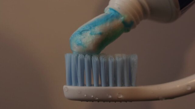 Close up of toothpaste being applied onto a toothbrush head in a bathroom setting, highlighting daily oral hygiene routine, cleanliness, and personal care. Soft lighting emphasizes fresh start concept