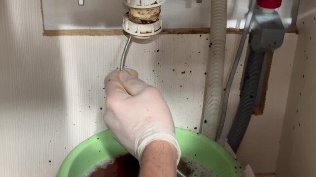 Plumber in gloves cleaning clogged kitchen sink drain with flexible snake tool