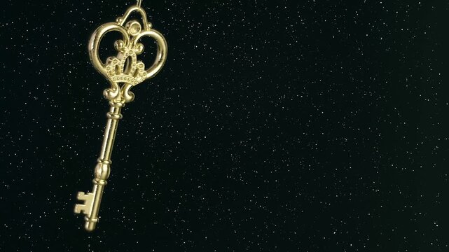 Beautiful decorative golden key on a string swings and rotates on a black background. View through sparkling particles. Closeup. Macro. Slow mo, slow motion, high speed camera, 200fps