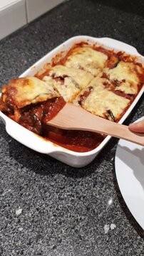 Vertical footage of a person using a wood spatula and taking out a portion of a homemade freshly baked eggplant parmigiana.
