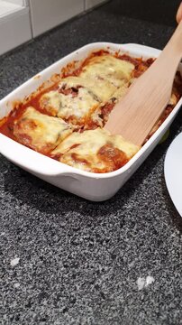 Vertical footage of a person inserting a wood spatula on a homemade freshly baked eggplant parmigiana.