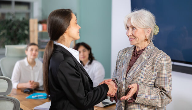 Senior female and girl participants of meeting end business negotiations with handshake, successful achievement of goals, mutual understanding, and reinforcement of deal with good relations..