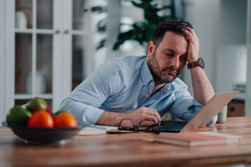 Obraz premium Man feeling exhausted and frustrated, holding his head while working from home, facing intense pressure and fatigue