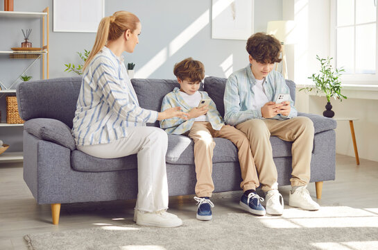 Young mother arguing with her children sitting on sofa addicted from mobile phone. Kids using smartphone playing online game ignoring parent at home. Technology and gadgets addiction problem.