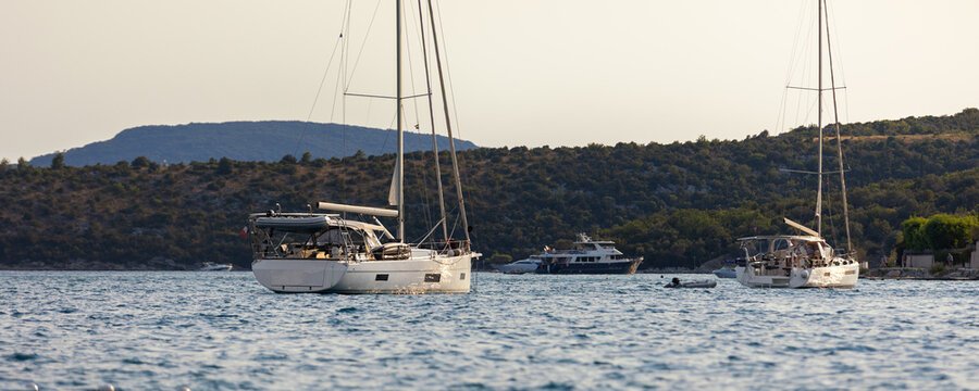 Sailboats anchored calm sea bay mediterranean coast green hills clear sky during warm summer evening. Scenic marine landscape yachts travel leisure atmosphere tranquil seaside tourism destination