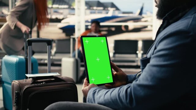 Vertical chroma key tablet in international airport terminal with diverse passengers relaxing in waiting lounge. Travelers with suitcases checking passports and plane tickets before journey.