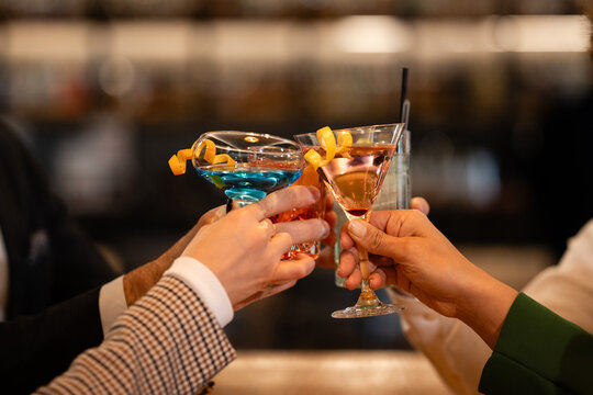 People raising cocktails cheering celebration at bar