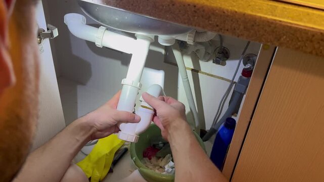 Plumber tearing off sealing tape and screwing pipe connection under kitchen sink