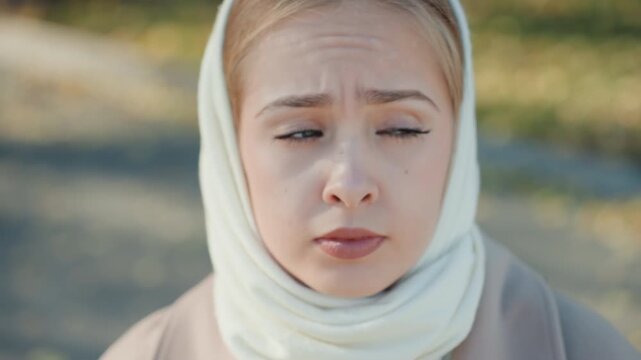 Young caucasian woman outdoors scarf pensive, student recollection, mother concern, witness silence, thinker pause closeup portrait with soft sunlight, shallow depth, autumn leaves, cool breeze, teary