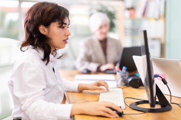 Fototapeta premium Young woman works on her laptop in group of women of different ages in office space