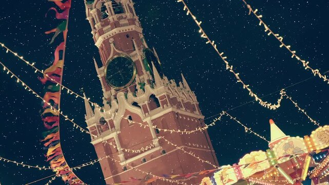 Festive garlands and a beautiful, colorful carousel against the backdrop of the Kremlin Spasskaya Tower with a clock on Red Square create a fun, New Year's mood. View through sparkling particles