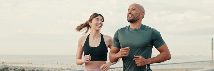 Obraz premium Close-up of young couple of athletes wearing sportswear running on the seafront outdoors. Panoramic