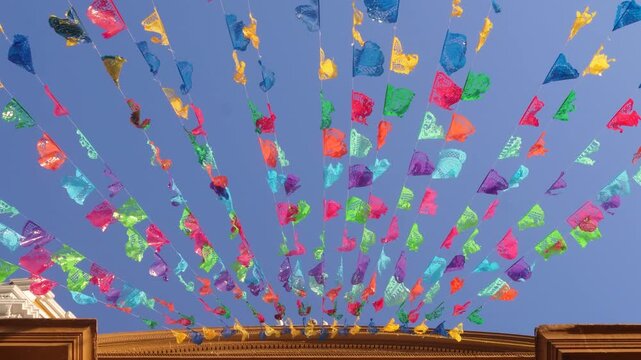 Vibrant papel picado waving from a building against a blue sky.