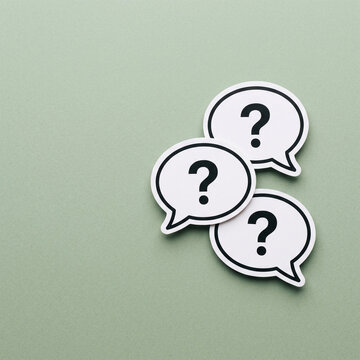 A trio of pristine white speech bubbles, prominently featuring bold black question marks, rests upon a soothing green surface, representing the essence of questioning, critical thinking,.