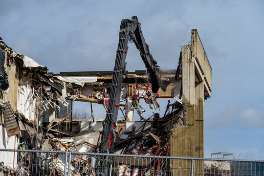 Urban redevelopment, hydraulic jaw of cracker attachment tearing down and demolishing an old concrete office building, heavy duty construction equipment at work on project

