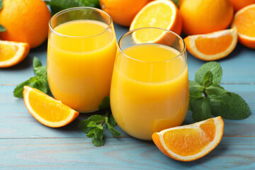 Citrus juice in glasses, fresh oranges and mint leaves on light blue wooden table, closeup © New Africa
