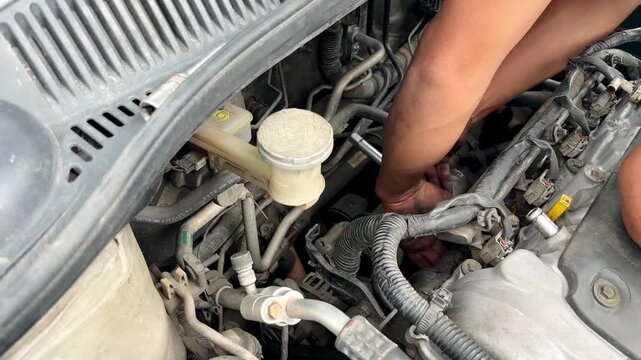 Mechanic hands repairing car engine under open hood. Automotive maintenance and repair concept with close up view of engine components.