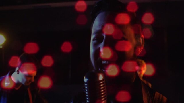 Lead vocalist stepping into mic while band performing, camera moving, red hexagonal bokeh filtering