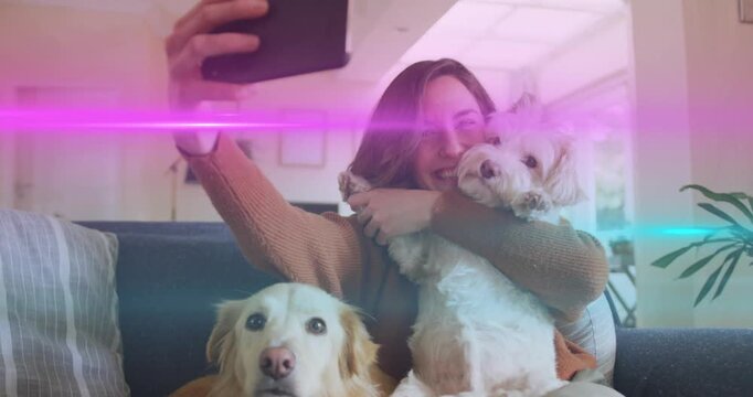 Extending left arm, woman in brown sweater holding phone, positioning dogs at home capturing selfie