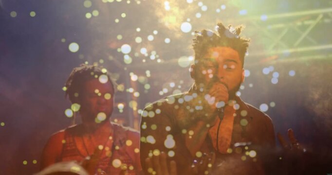 Lead singer raising wired mic and singing, engaging music crowd, backing moving, bokeh hiding faces