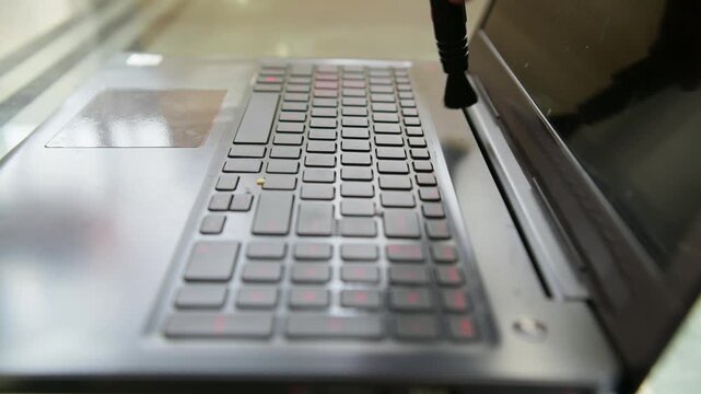 Cleaning dust from a laptop keyboard with a small brush.