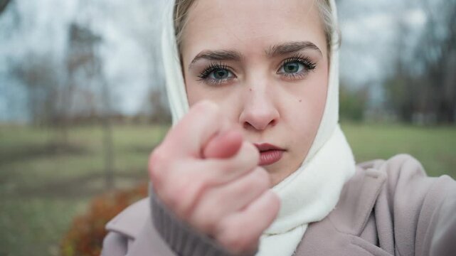Confident woman speaking. Assertive woman addresses camera with winter scenery backdrop strongly. Selfassured woman confidently communicates imperative message against winter trees background