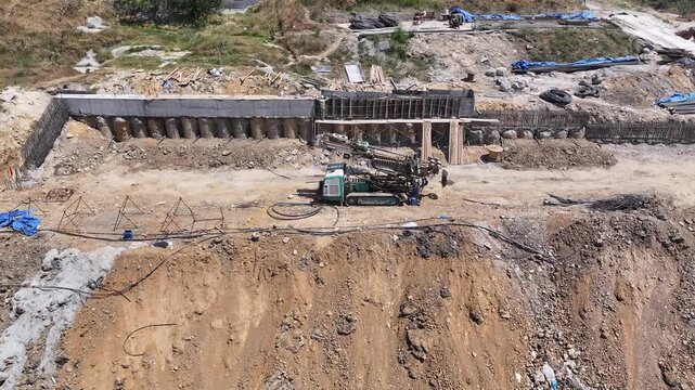 Piling rig working for foundation reinforcement in open field, reinforced concrete wall construction, and excavation area. Ground improvement and infrastructure project.
