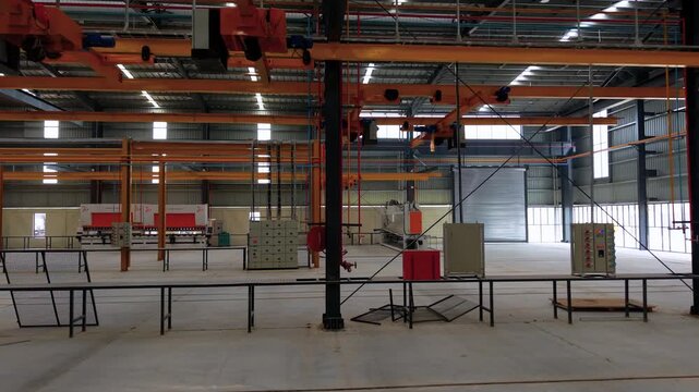 Wide shot of a large empty industrial warehouse featuring yellow overhead gantry cranes and production lines. Ideal for manufacturing, logistics, and engineering industry concepts.