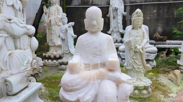 A collection of white marble Buddha statues are displayed in a garden in Ngu Hanh Son, Da Nang, Vietnam. These statues represent peace and are popular souvenirs for tourists.