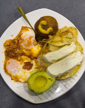 Traditional Medell&iacute;n Colombian breakfast with arepa, cheese, eggs, avocado and fried potato slices on white plate