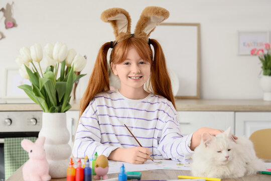 Cute girl with adorable cat and bunny ears painting at home. Easter celebration