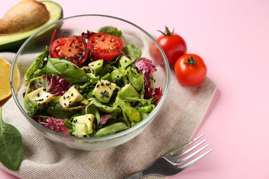 Glass bowl of tasty avocado salad with cherry tomatoes on pink background