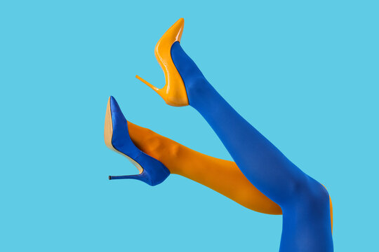 Legs of young woman in colorful tights and high heels on blue background
