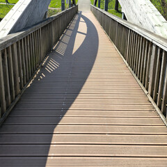 Fototapeta premium Sunlit Wooden Boardwalk Bridge with Geometric Shadow Patterns in a Park Setting