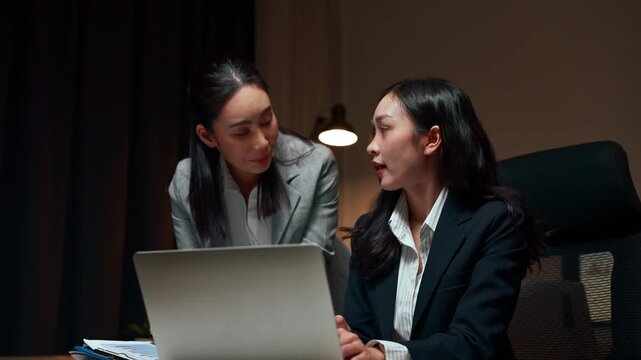 Two asian businesswomen collaborating on laptop at night