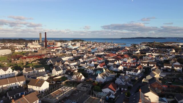St Sampson Guernsey high distant reveal over the rooftops of St Sampson past power station and backwards in golden afternoon sun with Vale Castle and Herm in the background