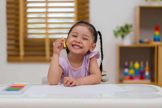 happy preschool child girl drawing and painting with colorful oil pastels on paper