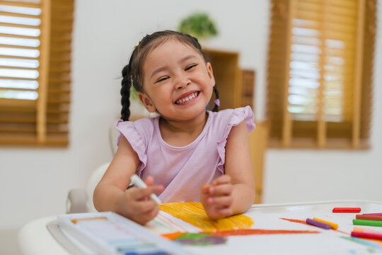 happy preschool child girl drawing and painting with colorful oil pastels on paper
