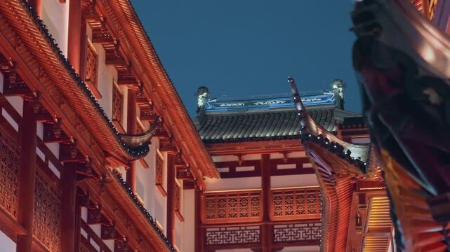Ornate red temple eaves at dusk, closeup of carved wooden roofline with gilded brackets and layered tiles calm twilight sky, intricate joinery and quiet courtyard, visitor admiring historic facade