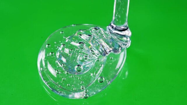 Viscous clear liquid dripping and forming a blob on a vibrant green surface