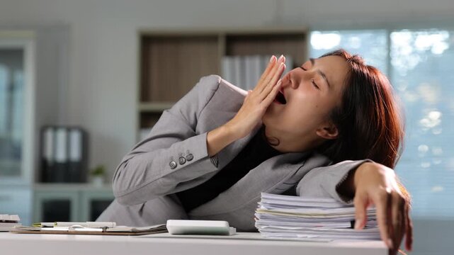 Overworked tired Asian businesswoman yawning and sleeping on a stack of documents.
