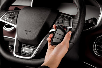 Obraz premium Woman holding modern car key, alarm system and steering wheel with electric buttons - female hands