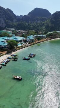 Vertical aerial drone orbit revealing tropical beach coastline with longtail boats and island mountains cinematic view 4K