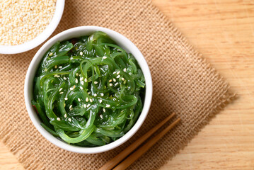 Fresh Japanese seaweed salad (Chuka Wakame) in a white ceramic bowl and chopsticks on wooden background, Table top view © nungning20