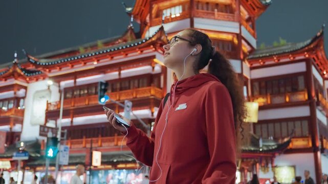 City night scene with red hoodie navigating crowded temple plaza while holding phone and earbuds shots alternate between vlogger streaming, navigator checking map app, content creator framing neon